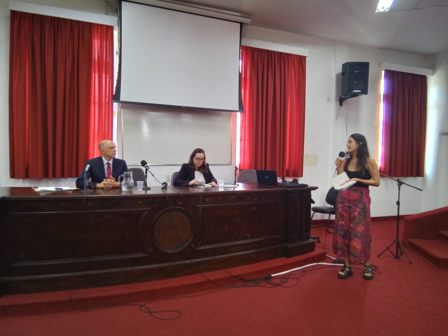 Na foto, a participação de uma representante de movimentos sociais no seminário. Ricardo Perlingeiro e Mariana Trotta ouvem a participante.